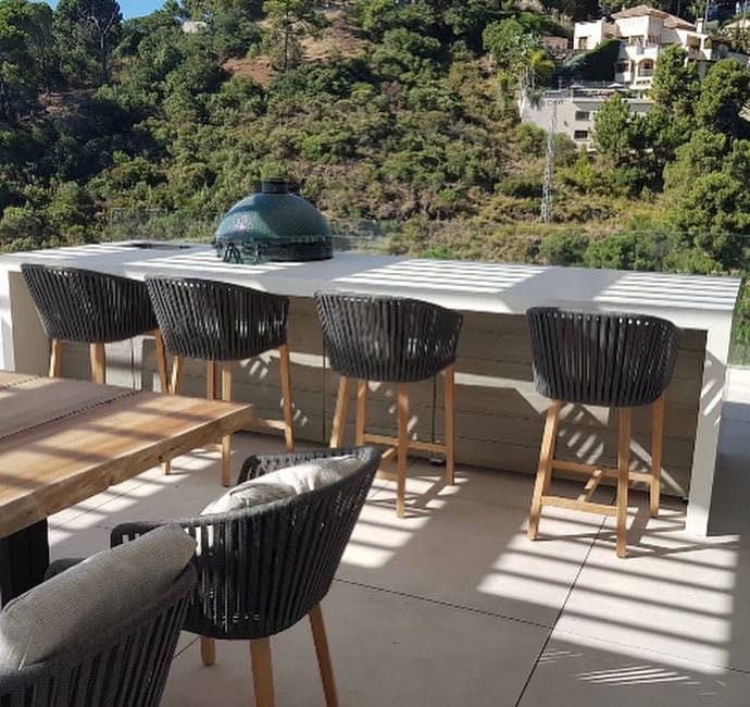 Green ceramic kamado grill on an outdoor bar with stools