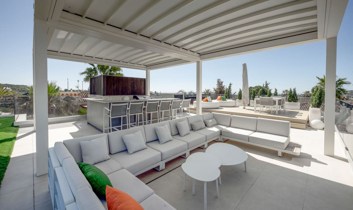 Rooftop terrace with a white louvred aluminium pergola, lounge sofas and an outdoor kitchen bar