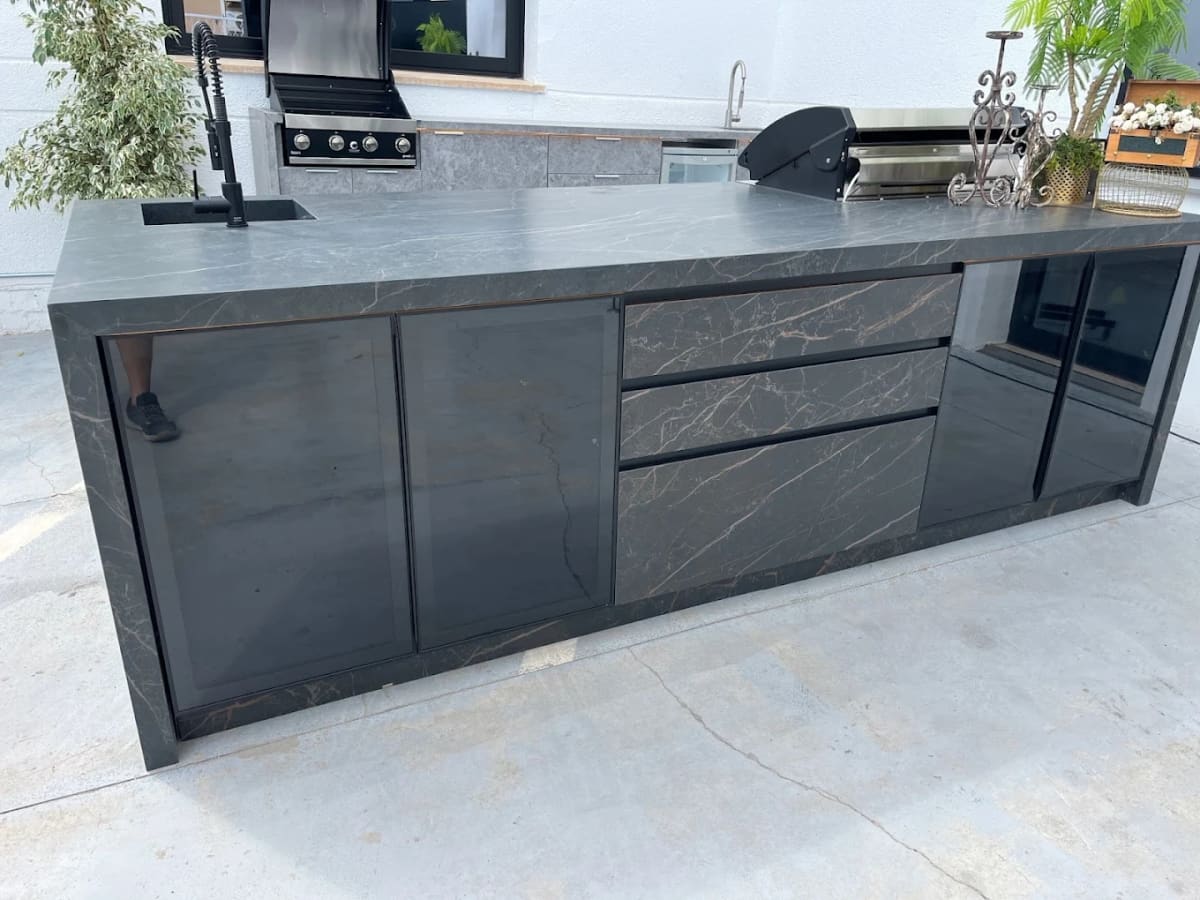 Outdoor kitchen island in dark veined sintered stone with sink, drawers and built-in BBQ
