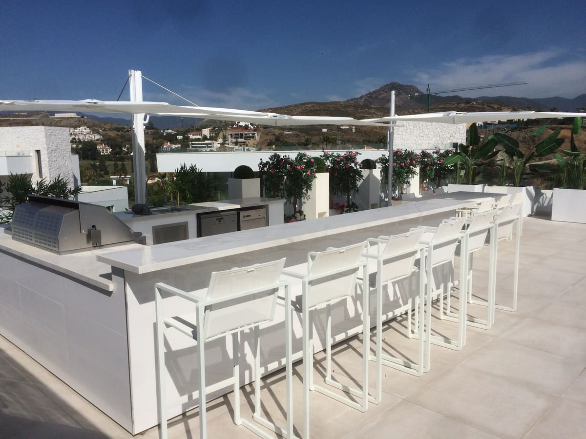 Long white outdoor kitchen bar with eight bar stools and a built-in BBQ on a terrace with mountain views