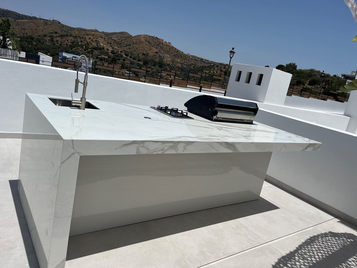 White marble-effect outdoor kitchen island with sink, gas hob and grill on a rooftop terrace in the hills