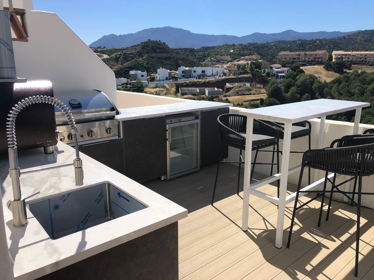 Compact outdoor kitchen with sink, gas BBQ and drinks fridge on a penthouse terrace overlooking the mountains